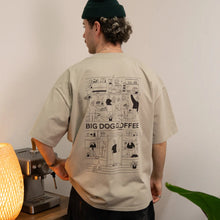 Cargar imagen en el visor de la galería, Person wearing a beige t-shirt with 'BIG DOG COFFEE' graphic design, standing in a room with a lamp and plant.